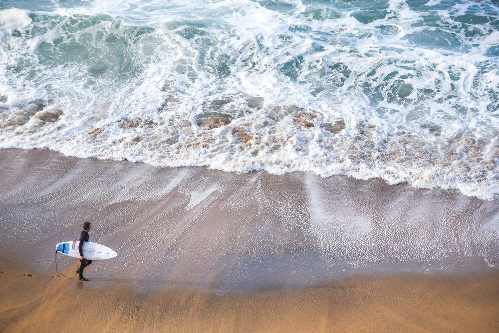 surfer man on the beach with turquoise-white water wave in the sea from top view at Bells beach