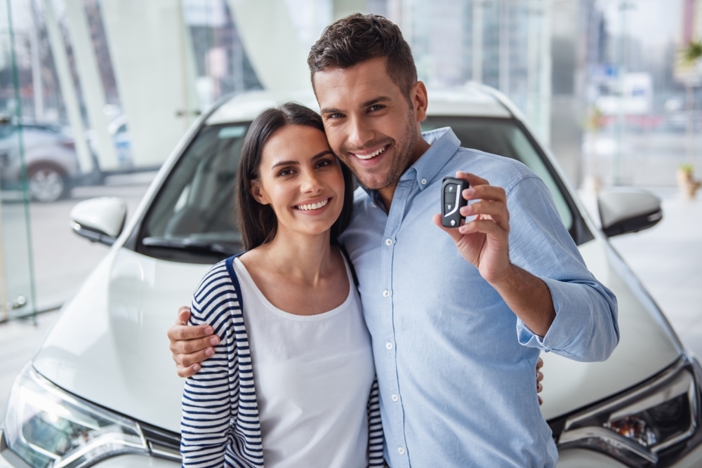 Beautiful couple is holding a key of their new car, looking at camera and smiling