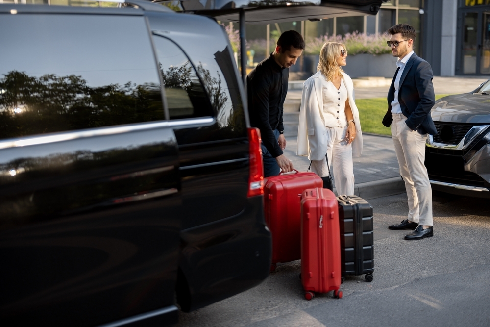 Business couple standing by a minivan taxi waiting for their chauffeur or porter to help them with a suitcases