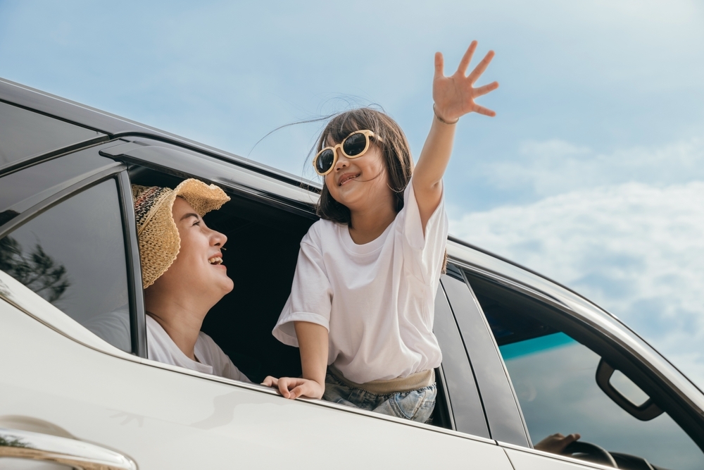 Dad, mom and daughter little kid smiling sitting in compact car windows raise hand wave goodbye