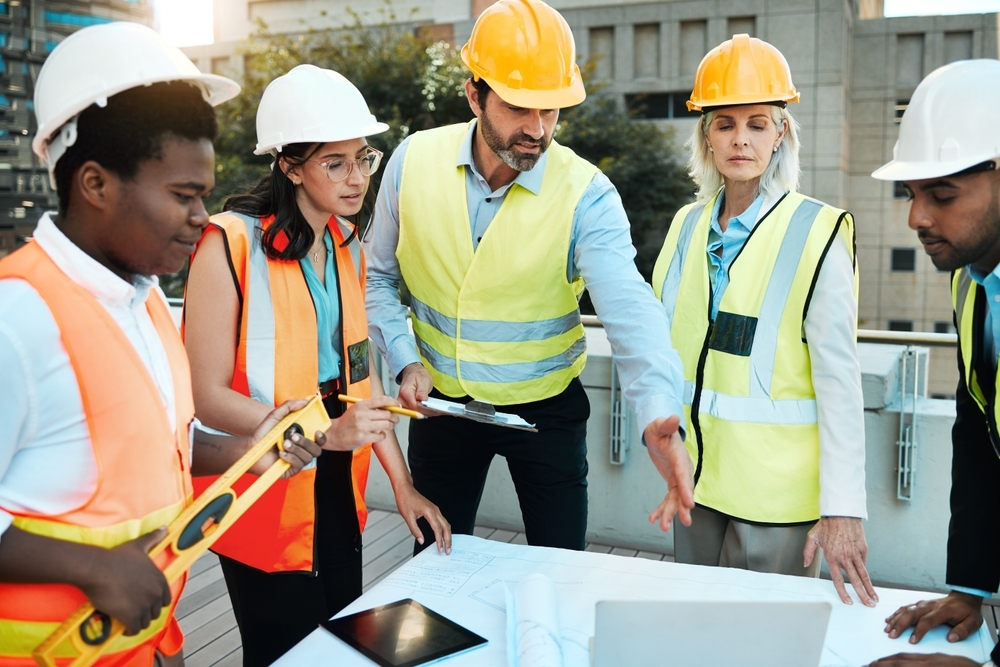 diverse group of contractors standing outside together and having a discussion over building plans