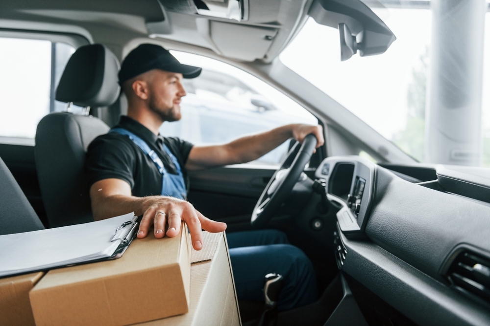 Modern vehicle. Delivery man in uniform is indoors with car and with order.