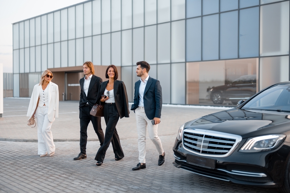 Group of business people talking on the go from modern building of airport or some office to luxury taxi on parking lot