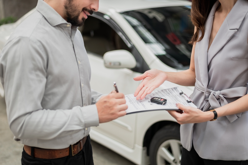 Happy customer with car dealer agent making deal and signing on agreement document contract