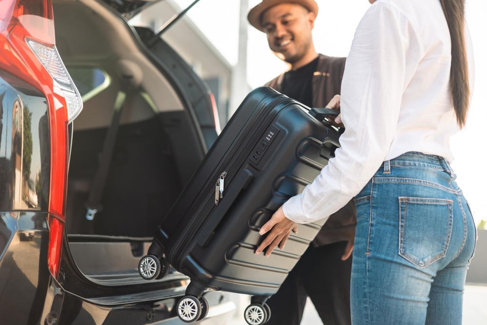Happy couple puts his suitcase in the back of the car